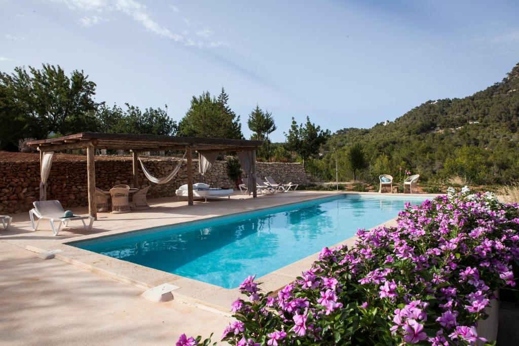 una piscina con cenador y flores púrpuras en Hacienda Ses Caletes, en Cala San Vicente