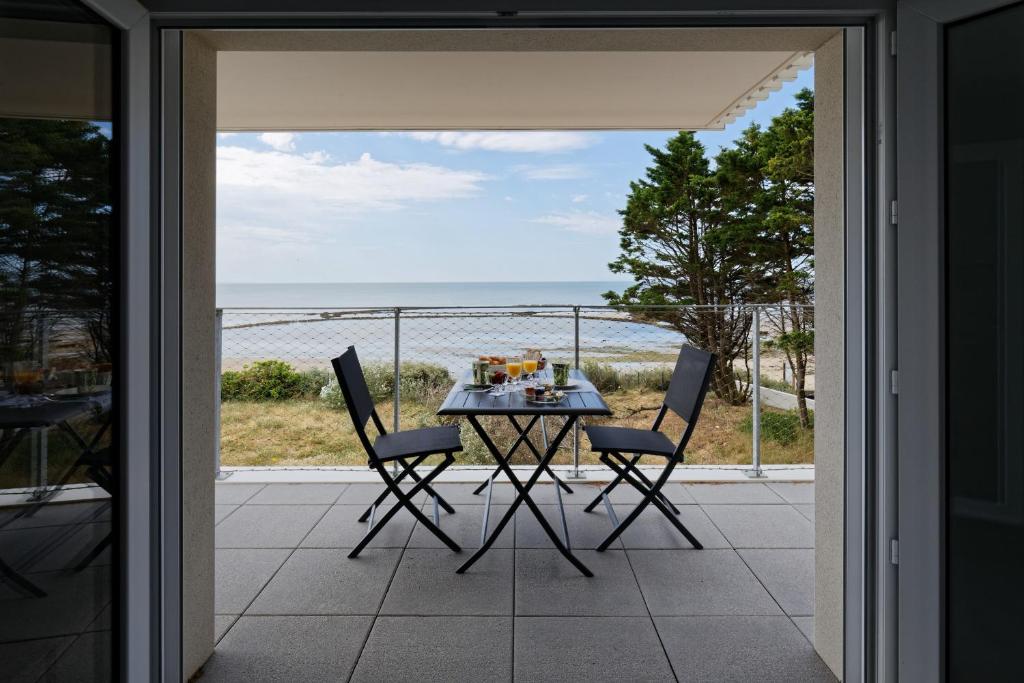 Superbe appartement neuf face plage sur l ile de Noirmoutier في La Guérinière: طاولة وكراسي على شرفة مطلة على المحيط