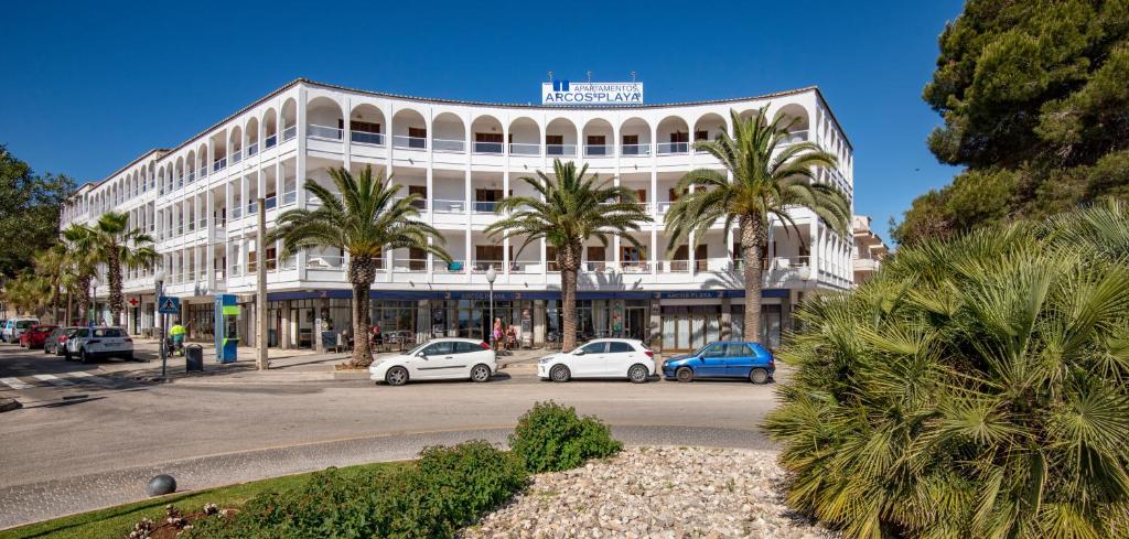 un grand bâtiment blanc avec des palmiers devant lui dans l'établissement Apartamentos Arcos Playa, à S'illot