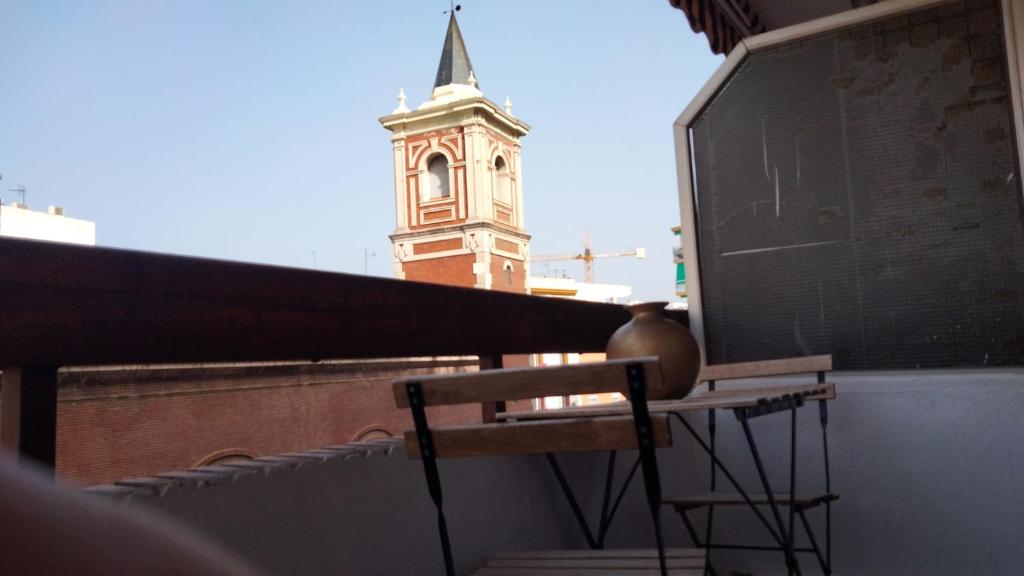 una mesa y una silla en un balcón con una torre del reloj en Triana Luck, en Sevilla