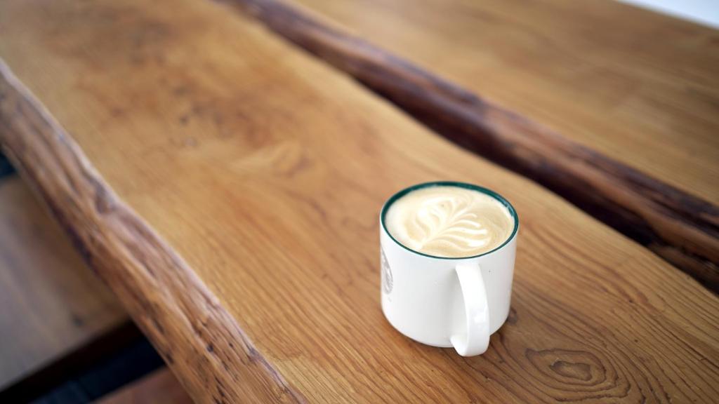 a cup of coffee sitting on a wooden table at It's Mine Hostel in Taitung City