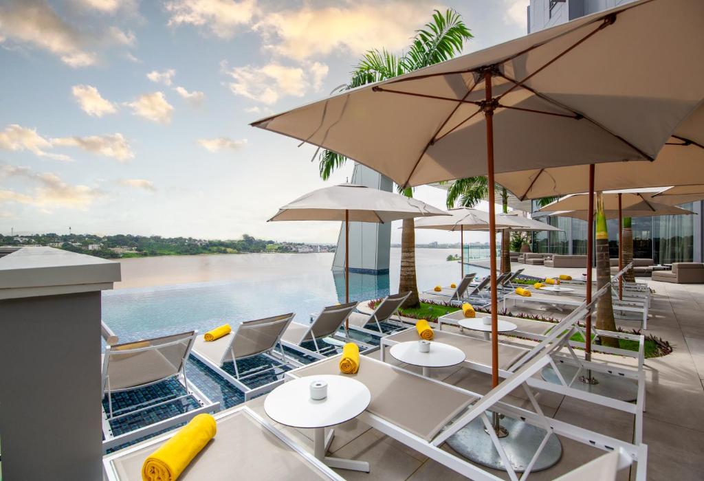a patio with tables and umbrellas and the water at Noom Hotel Abidjan Plateau in Abidjan