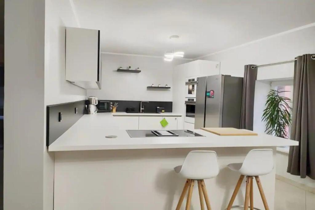 una cocina con encimeras blancas, armarios y taburetes blancos en Modern 3 bedroom apartment near Useldange castle, en Useldange
