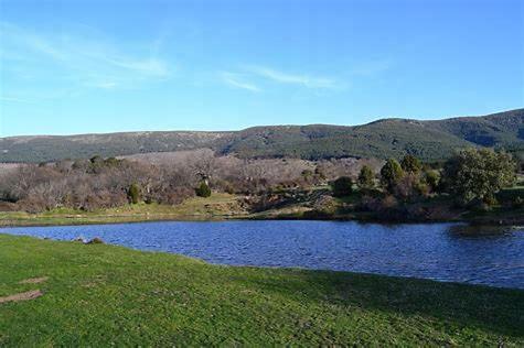un lago en medio de un campo con montañas en el fondo en hostal Decerca Prádena, en Prádena