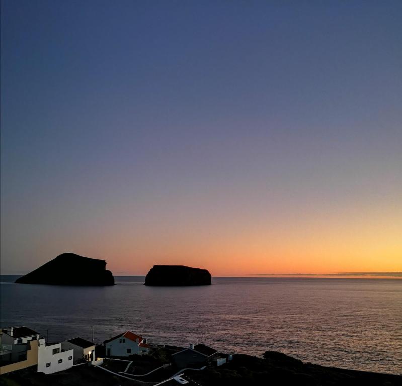 a sunset over the ocean with two islands in the water at Breathe Nature - Beach House Azores in Feteira