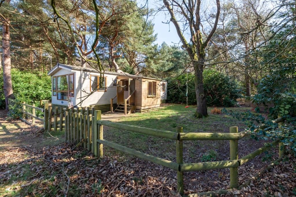 una cabina nel bosco con una recinzione di Beechcroft - Norfolk Cottage Agency a Holt