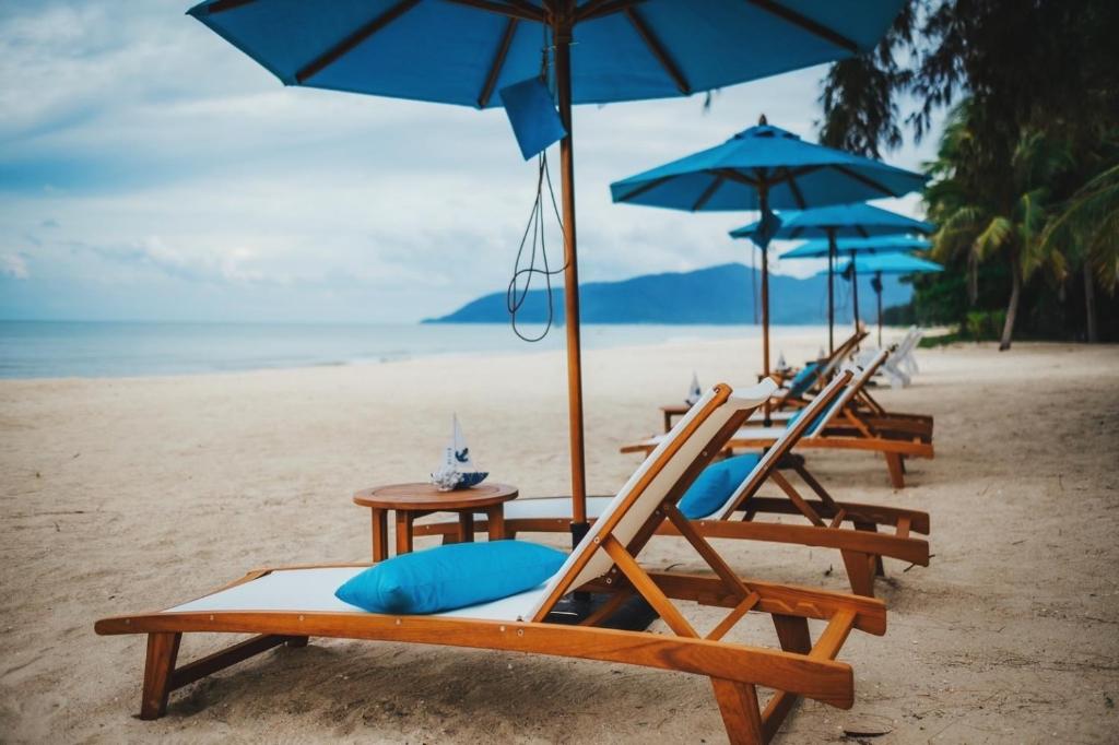 eine Reihe von Liegestühlen mit Sonnenschirmen am Strand in der Unterkunft Khanom Sea Beach Resort in Nakhon Si Thammarat
