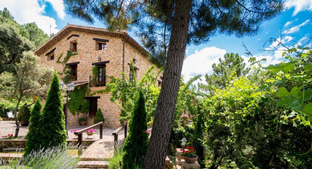 una antigua casa de piedra en un jardín con árboles en Hotel de Montaña Cueva Ahumada, en Villaverde de Guadalimar