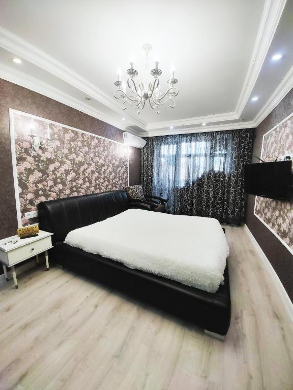 a bedroom with a black bed and a chandelier at Красивый однокомнатный люкс в районе вокзала in Karagandy