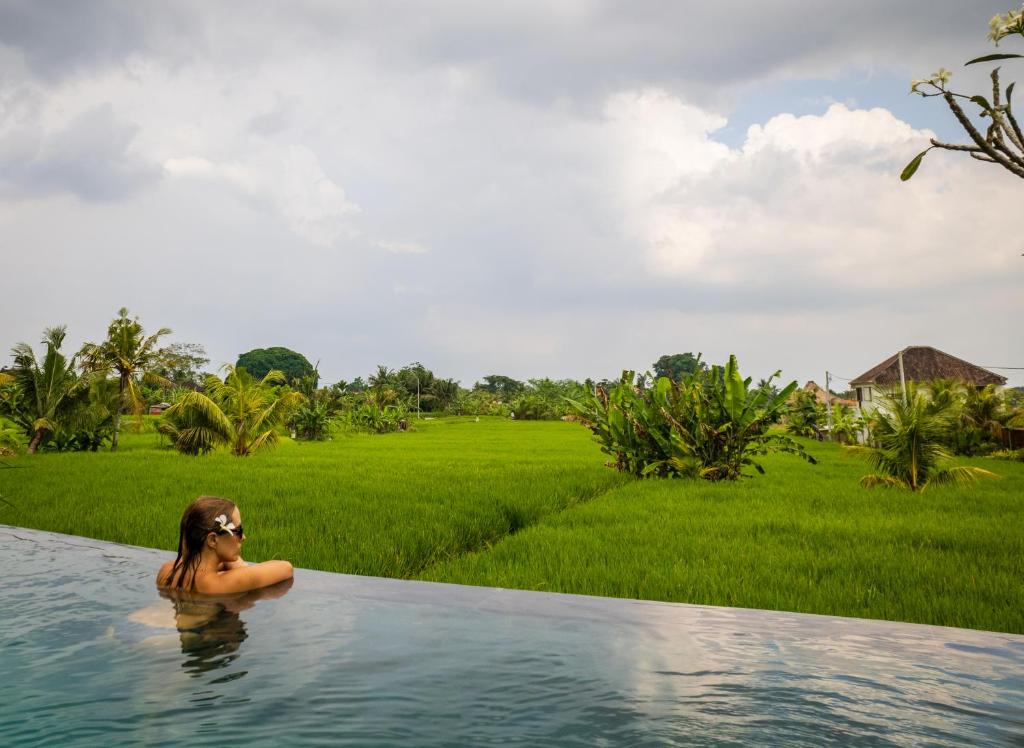 una mujer en una piscina frente a un campo en Uma Jala Villa Ubud en Ubud