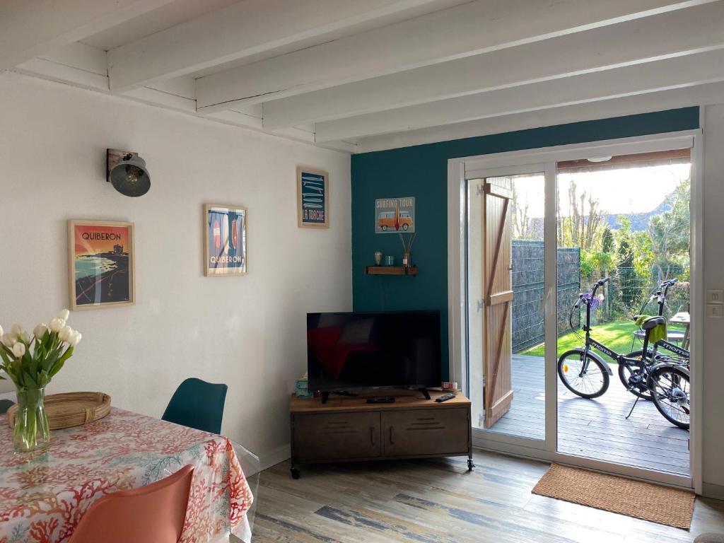 ein Wohnzimmer mit einem Tisch, einem TV und einem Balkon in der Unterkunft 250 m des plages - Jardin - WIFI - Velos - in Carnac