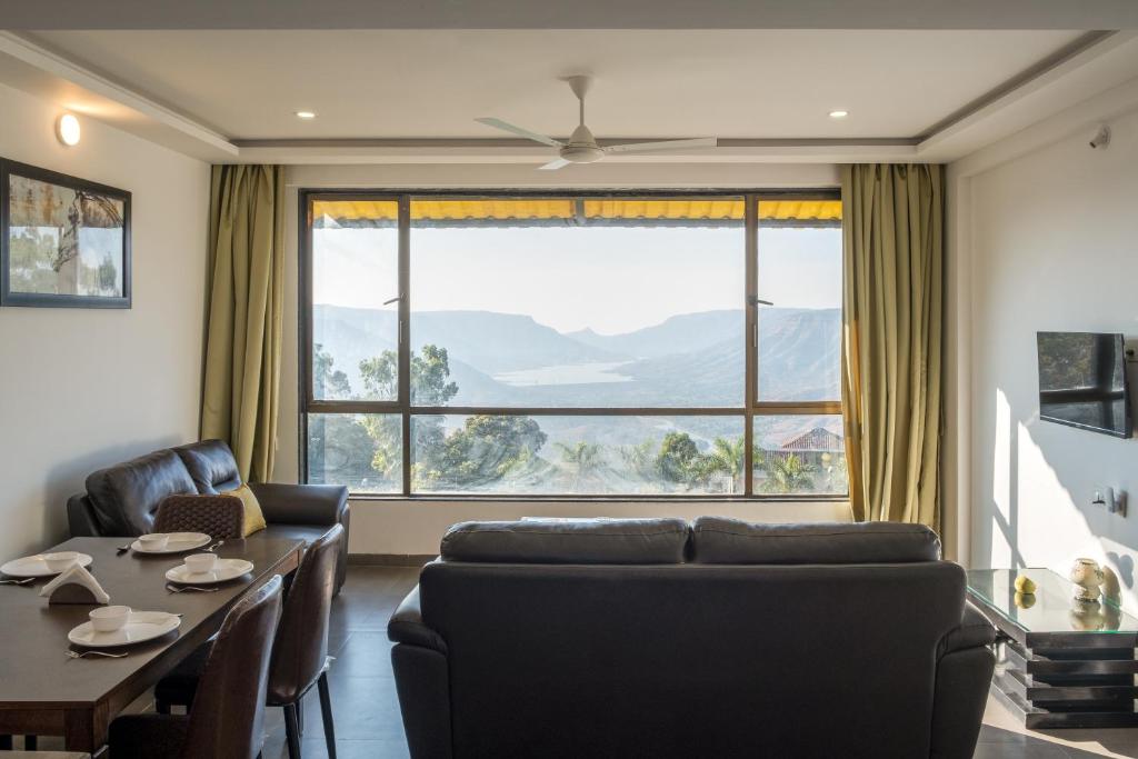 a living room with a couch and a table and a large window at West Valley Villa 3BHK B in Mahabaleshwar