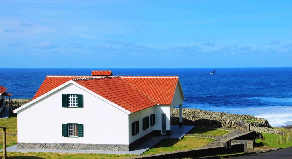 una casa blanca con techo naranja junto al océano en Casas da Cascata, en Lajes das Flores