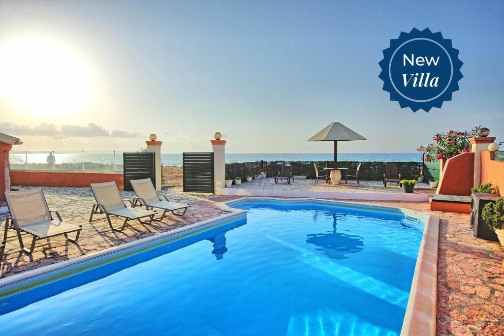 a swimming pool with chairs and the ocean in the background at Beach Villa Athanasia - villa with private pool on the beach by PosarelliVillas in Acharavi