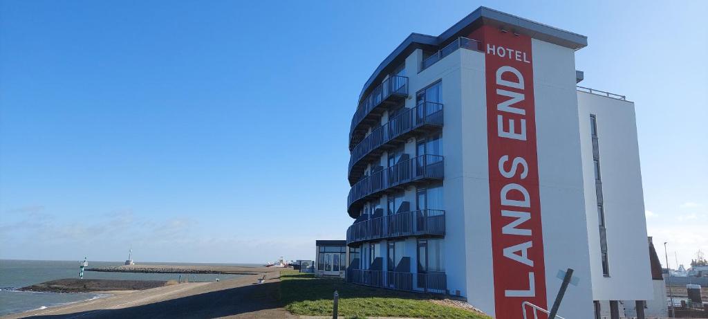 a building with a red and white sign next to the ocean at Hotel Lands End in Den Helder