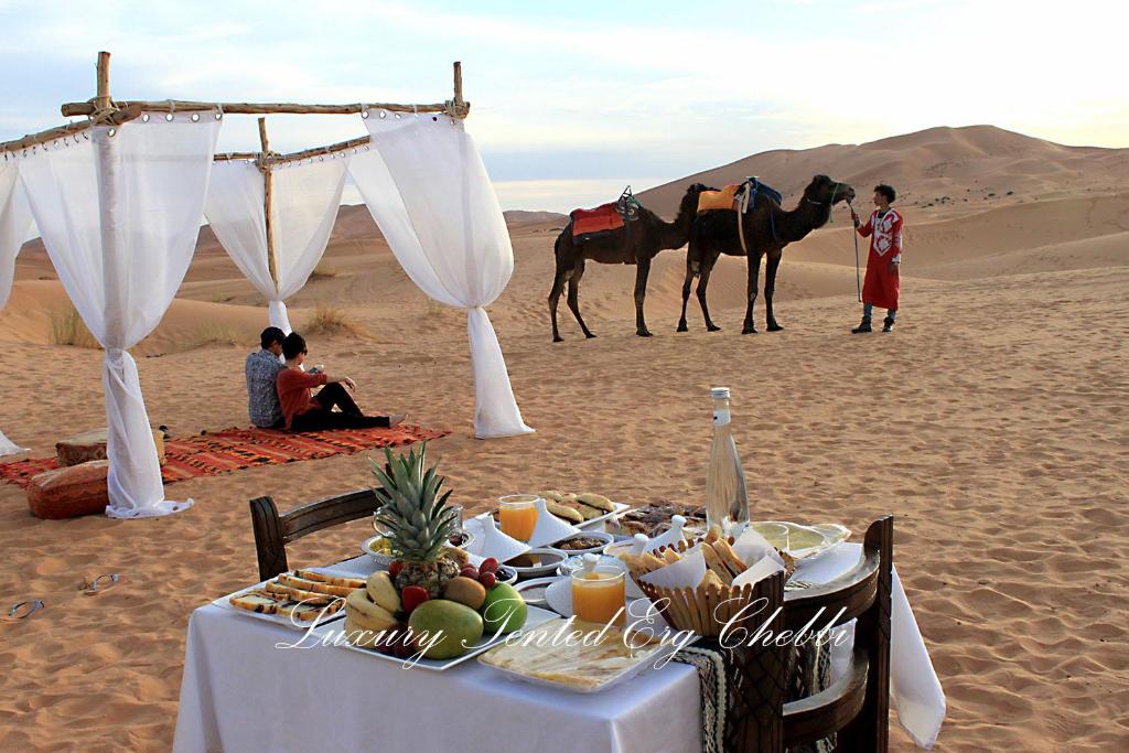 een tafel in de woestijn met een groep mensen en paarden bij Luxury Tented Erg Chebbi in Merzouga