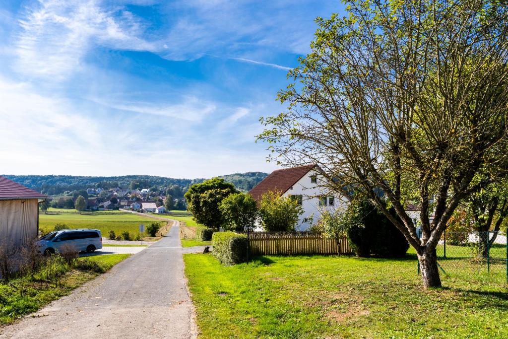 uma estrada que leva a uma fazenda com uma casa e uma árvore em Jura Ferienhof em Velburg