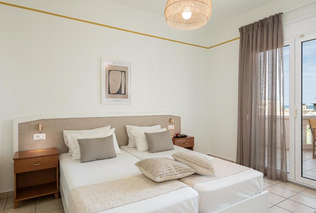 a white bedroom with a large white bed and a window at Artemis Apartments in Stalos