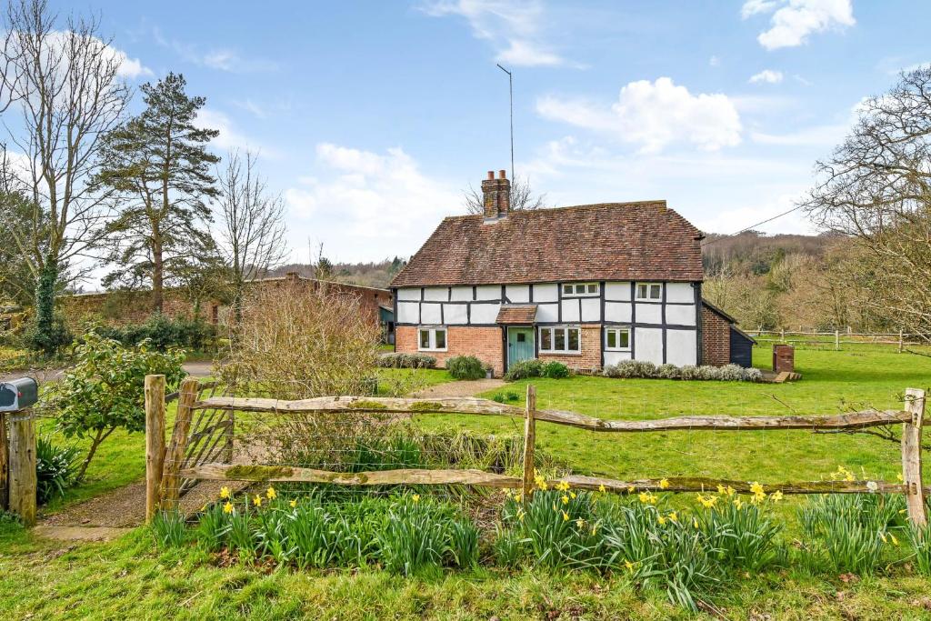 a house in a field with a fence and flowers at Bellflower Cottage, Ashdown Forest in Horsted Keynes