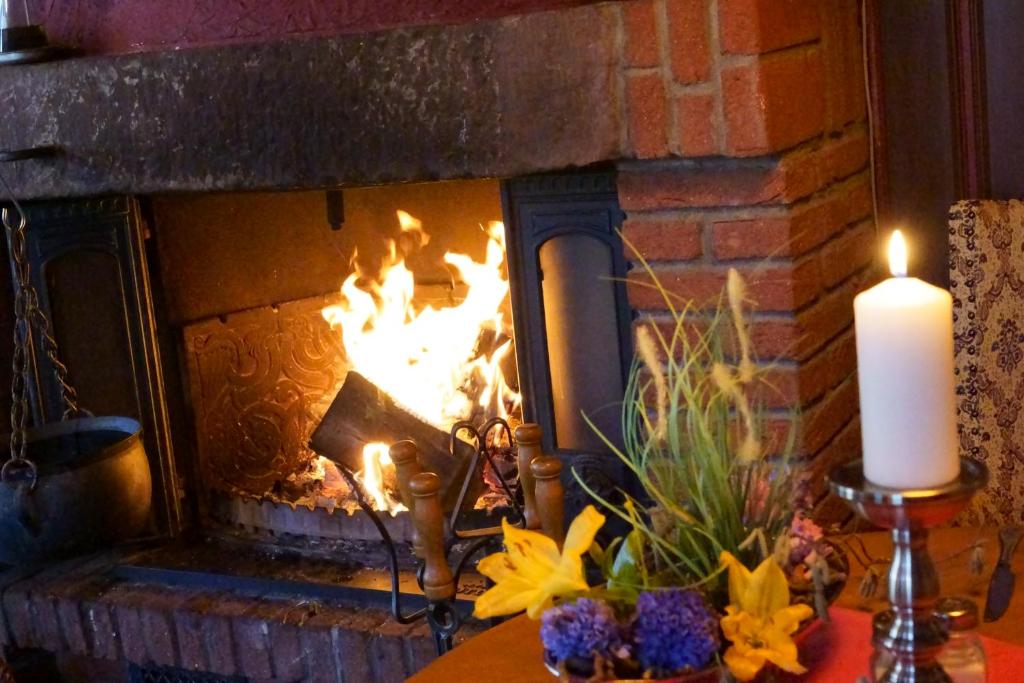 a fire in a brick fireplace with a candle and flowers at Landhaus Zum alten Fritz in Seesen