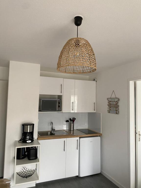 a kitchen with white cabinets and a pendant light at Cabourg T2 cosy avec accès direct plage in Cabourg