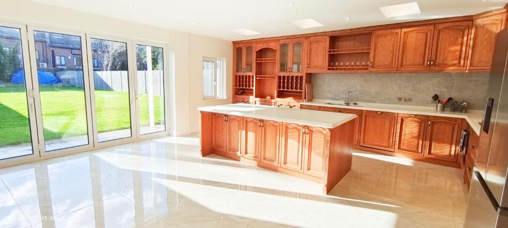 a kitchen with wooden cabinets and a large window at Marigold Villa in Harrow