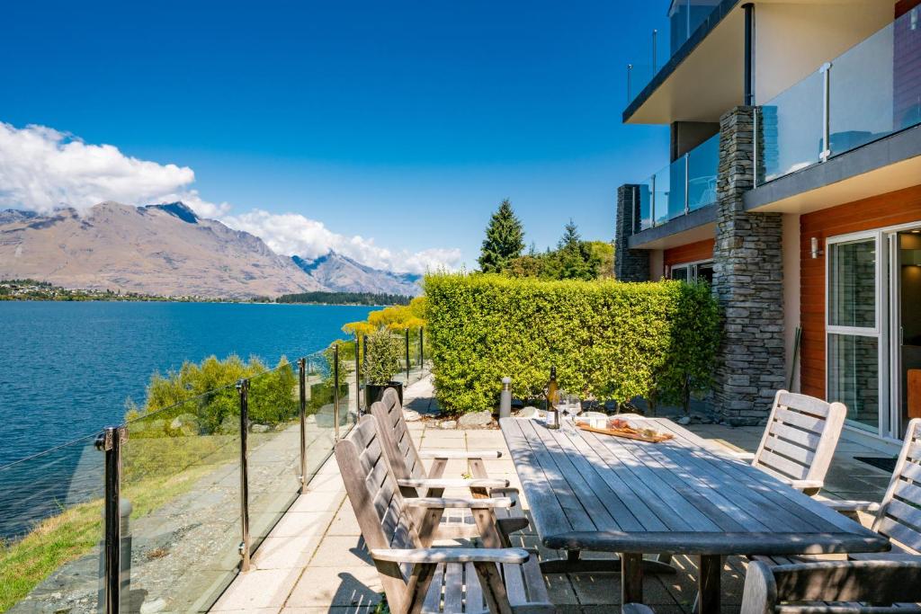 a wooden table and chairs on a patio next to the water at Lake Front 3-bedroom Apartment with Lake Access in Queenstown
