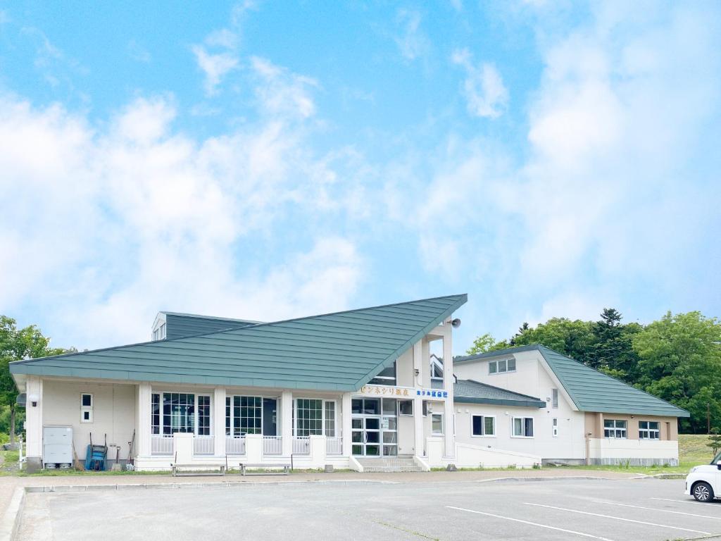 een wit gebouw met een groen dak op een parkeerplaats bij ピンネシリ温泉望岳荘 