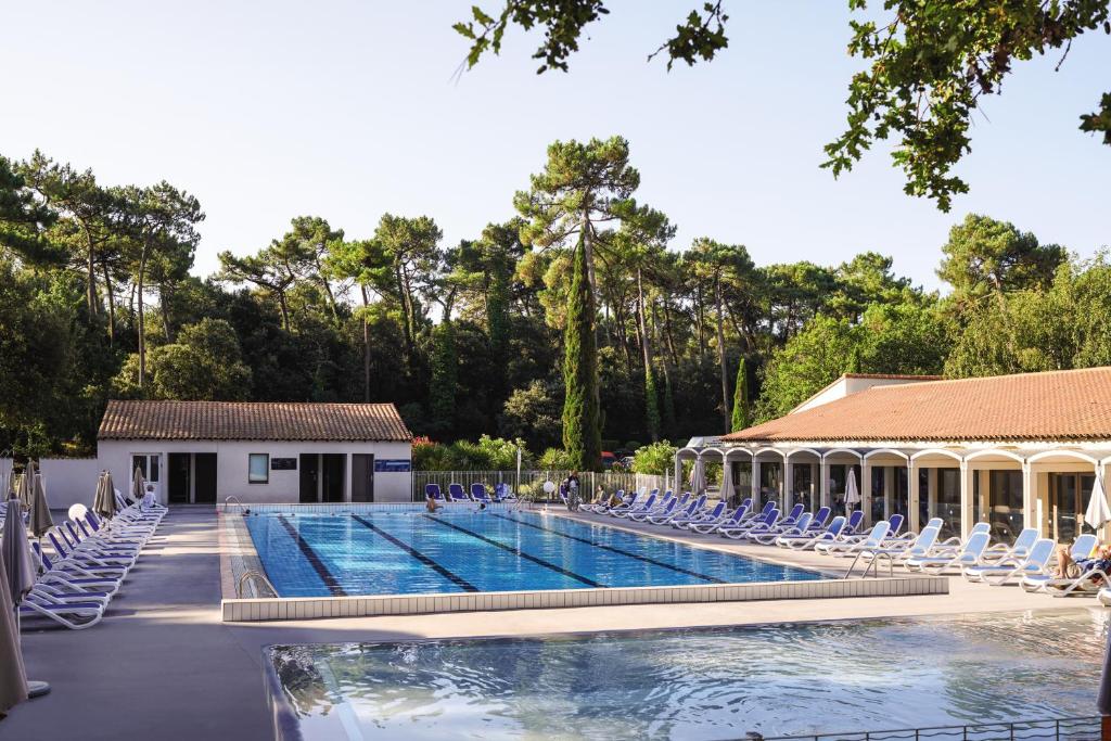 a swimming pool with chairs and a building at Belambra Clubs La Palmyre - Les Mathes in Les Mathes