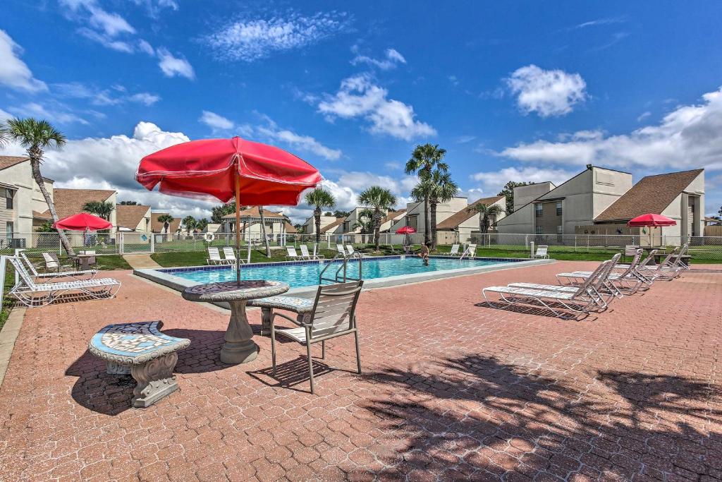 a pool with a table and chairs and a red umbrella at Cozy PCB Condo Less Than half Mile to Public Beach Access! in Panama City Beach