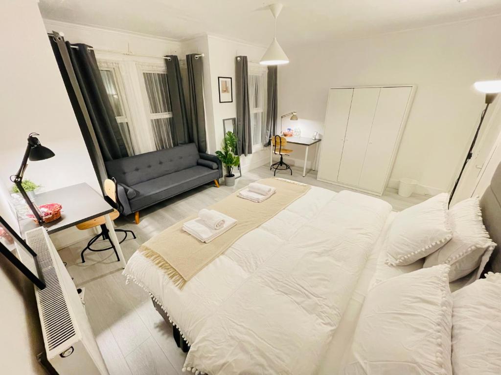 Cama blanca grande en habitación con sofá en Leytonstone House - SleepyLodge en Londres