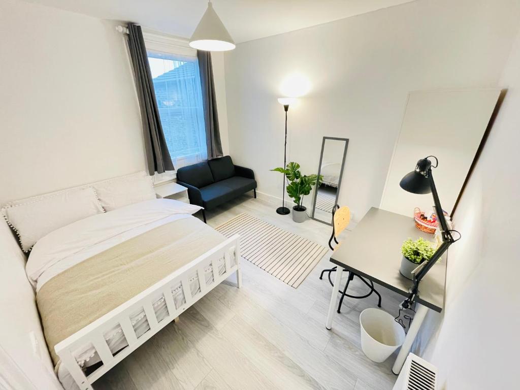 a white bedroom with a bed and a desk at Leytonstone House - SleepyLodge in London