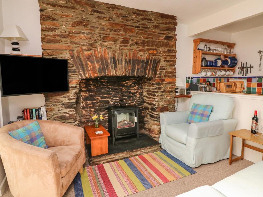 een woonkamer met 2 stoelen en een open haard bij Honeysuckle Cottage in Kingsbridge