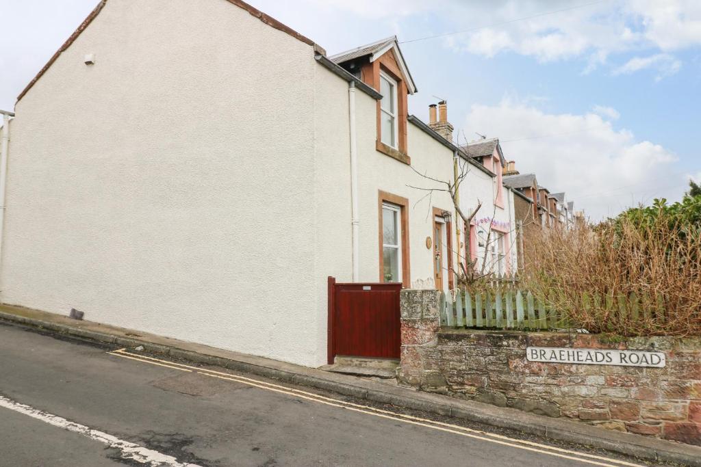 a white house with a red door on a street at 1 Blinkbonny Cottages in Saint Boswells