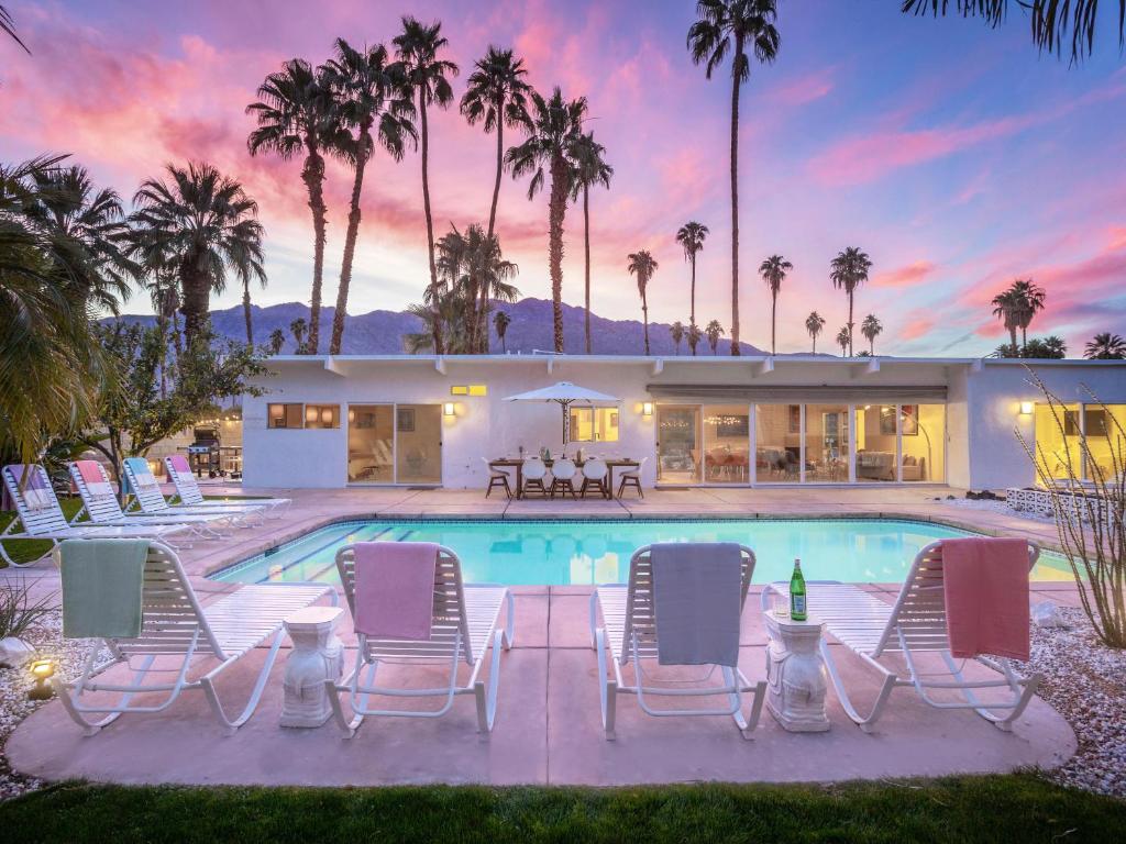 a pool with chairs and a house with palm trees at House of Stardust in Palm Springs