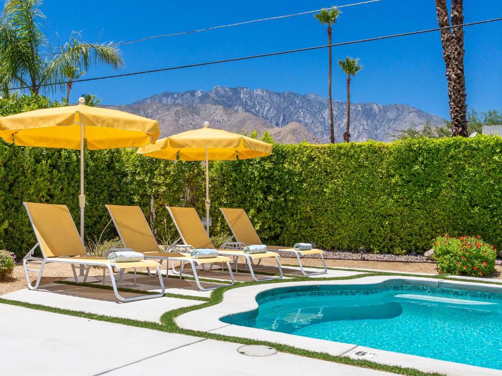 eine Gruppe von Stühlen und Sonnenschirmen neben einem Pool in der Unterkunft Mellow Yellow Butterfly in Palm Springs