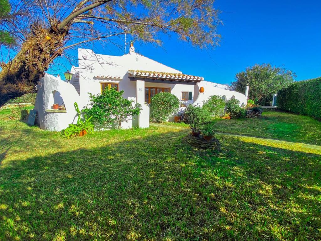 una casa blanca en un césped verde con un árbol en Villa con piscina privada y gran jardín, en Cala'n Bosch