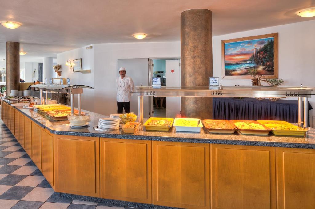 a man standing behind a buffet line of food at Corali Hotel in Tigaki