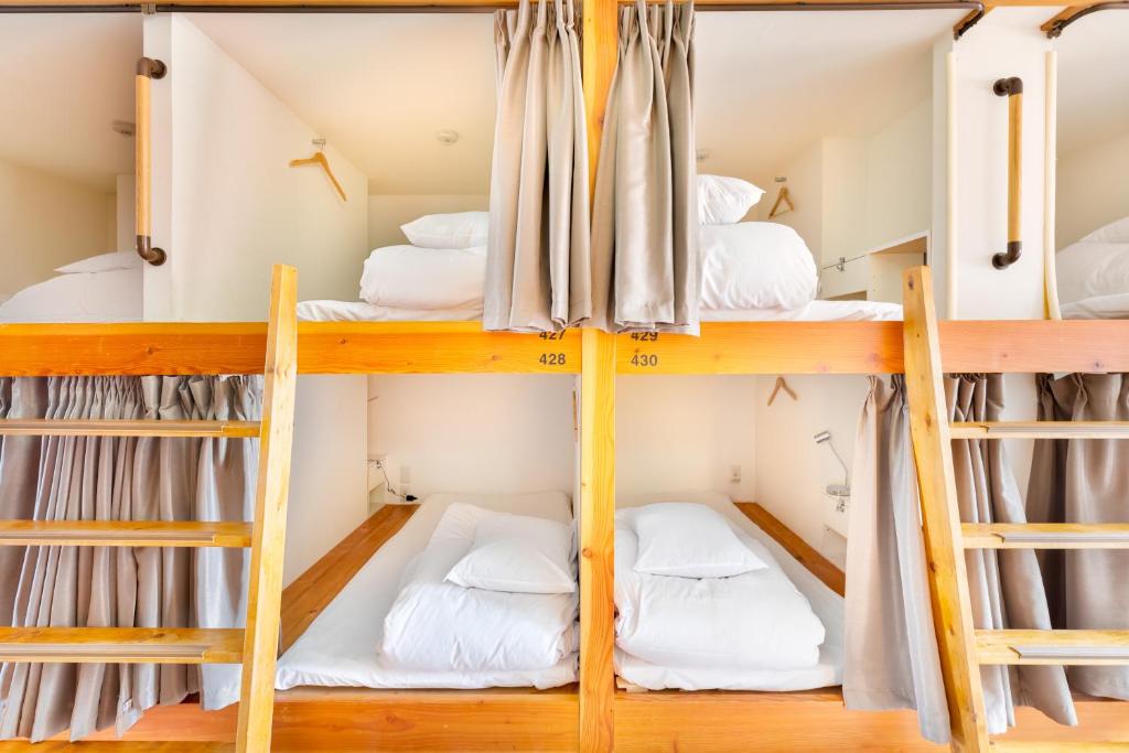Hostel OGK في أوساكا: أربعة أسرة بطابقين في غرفة نوم مع أسرة بيضاء