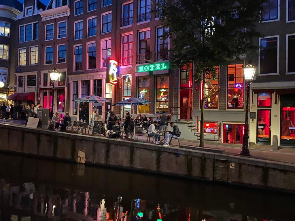 um grupo de pessoas sentadas em mesas à beira de um rio à noite em Hotel & bar Royal taste Amsterdam em Amesterdão
