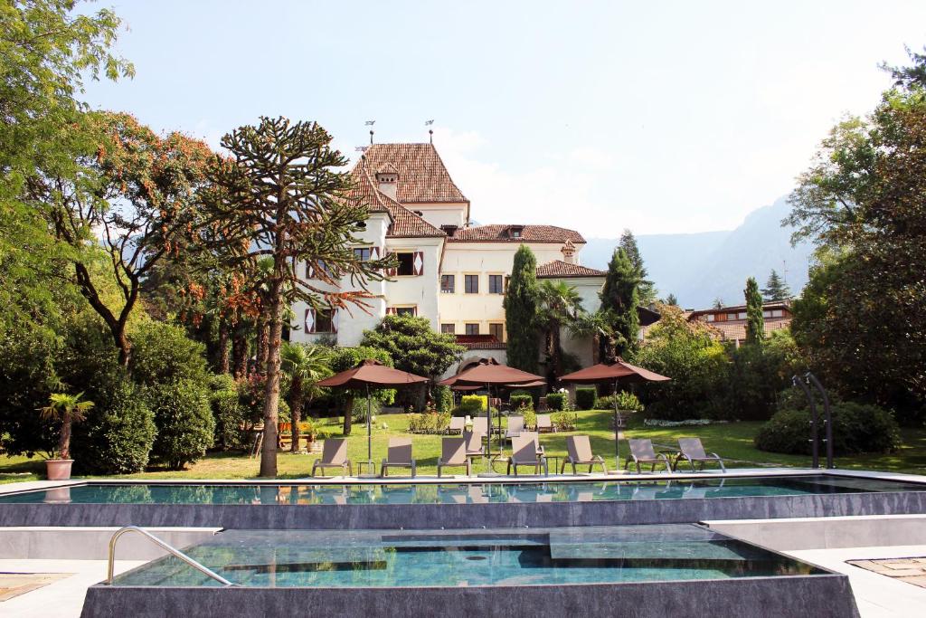 een resort met een zwembad en stoelen en een gebouw bij Hotel Castel Rundegg (Adults Only) in Merano