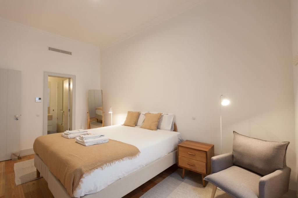 een witte slaapkamer met een bed en een stoel bij FLH Bacalhoeiros Spacious Apartment in Lissabon