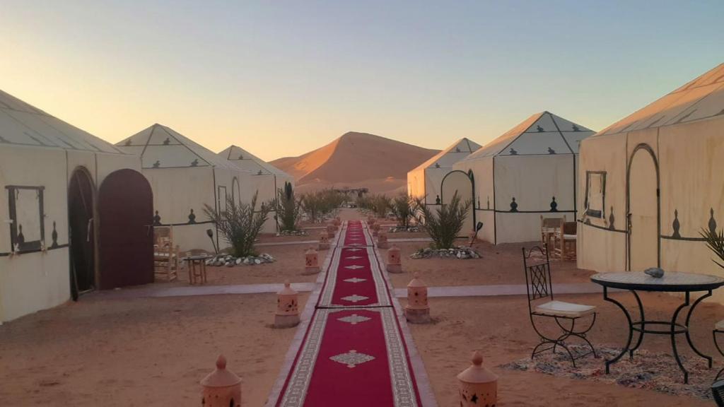 Sahara Tours luxury camp في مرزوقة: صف من المباني في صحراء مع طاولات وكراسي