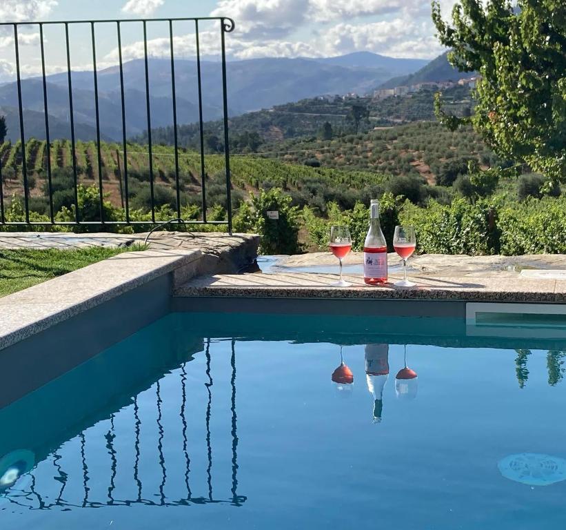 uma piscina com dois copos de vinho e vista em Quinta do Monte Travesso - Country Houses & Winery em Tabuaço