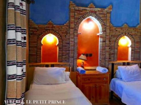 a bedroom with two beds and a brick wall at Hotel Riad Le Petit Prince in Merzouga