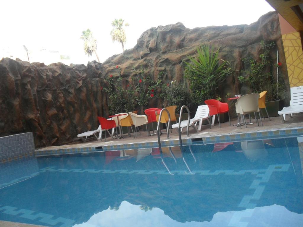 einen Pool mit Stühlen, einem Tisch und einer Felswand in der Unterkunft Hotel Gomassine in Marrakesch