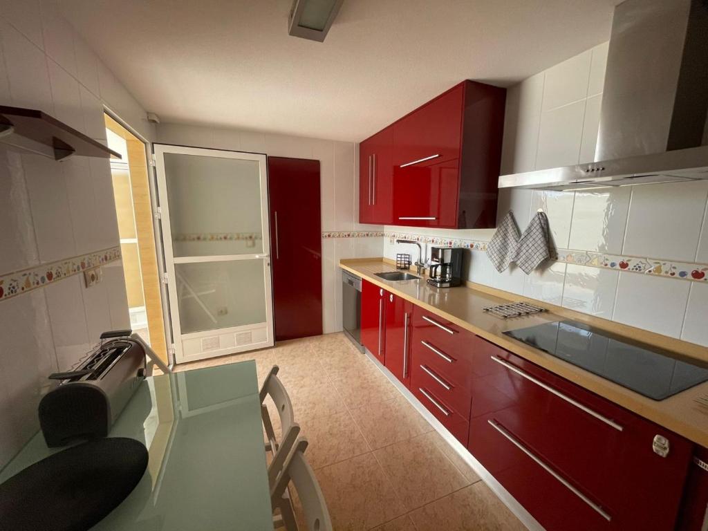 uma cozinha com armários vermelhos e uma mesa de vidro em Casa Moraira em Águilas