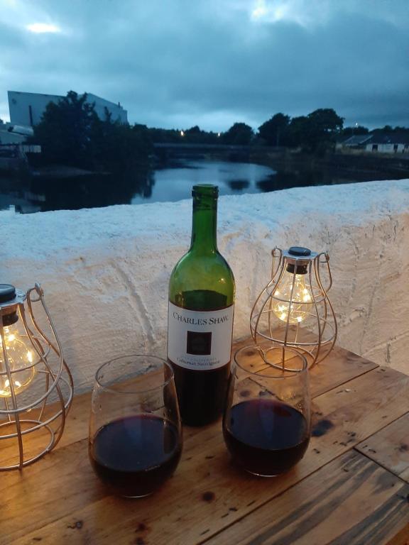 a bottle of wine and two glasses on a wooden table at Stunning Riverside Town House with views Ayrshire in Girvan