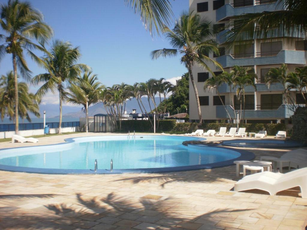 a swimming pool with palm trees and a building at Apartamento Beira Mar in Caraguatatuba