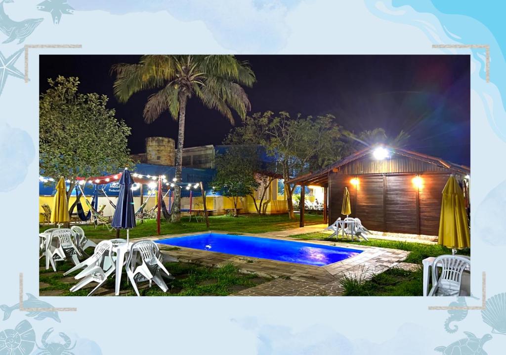 uma piscina à noite com mesas e cadeiras em Hostel Pedacinho do Céu em Itanhaém